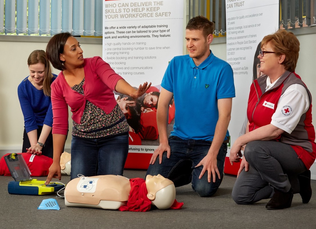 A British Red Cross tRainer is teaching three course attendees how to administer CPR.