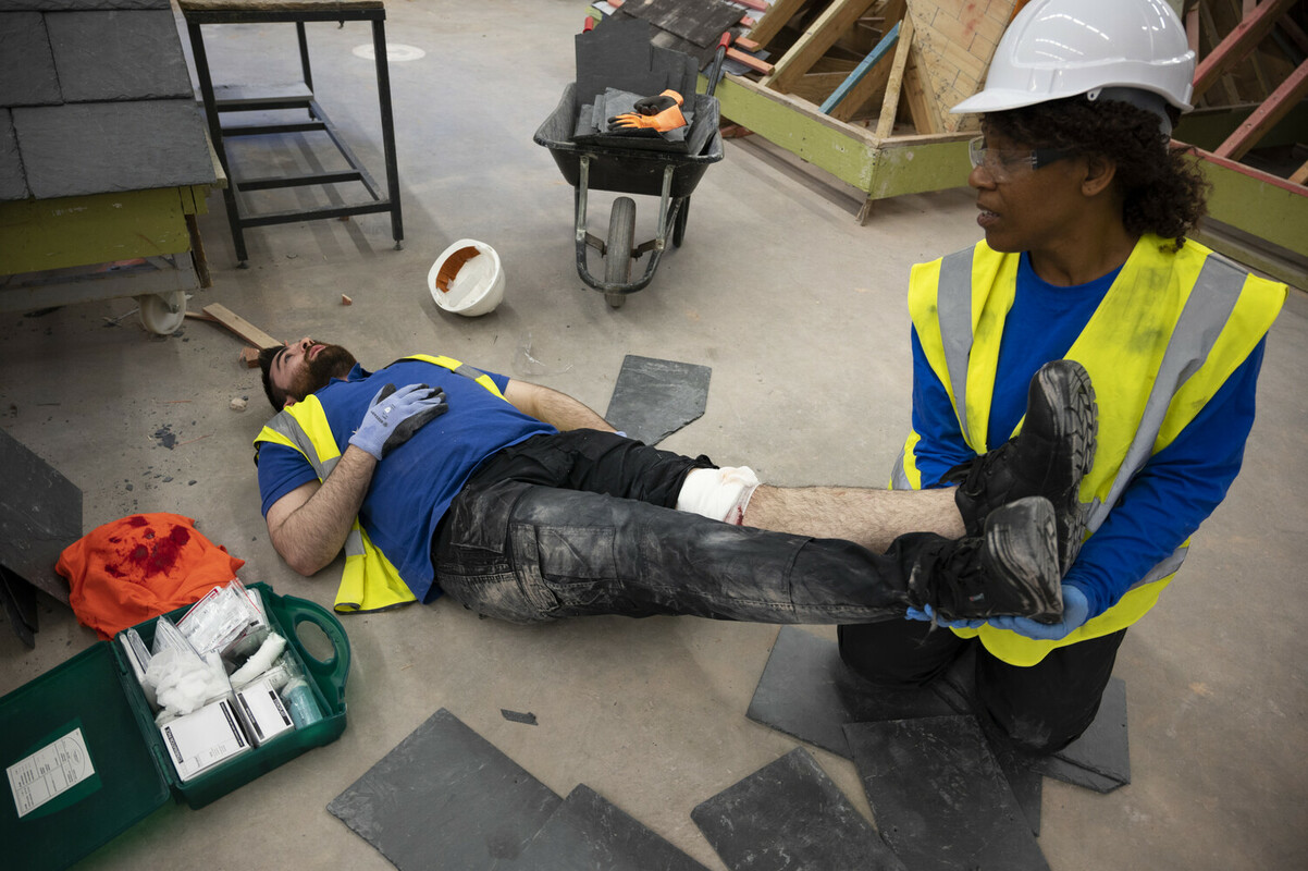 Two construction workers on site. One has had a leg injury, so it lay on the floor, while the other elevates his legs.