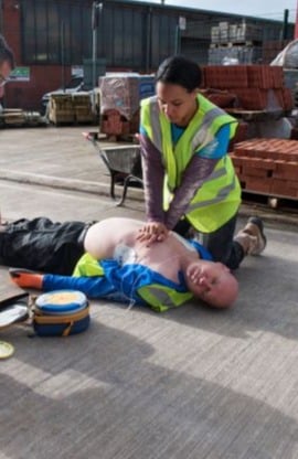 A construction worker on site, giving a member of their team CPR.